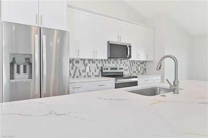 Kitchen with appliances with stainless steel finishes, a sink, decorative backsplash, white cabinetry, and light stone countertops