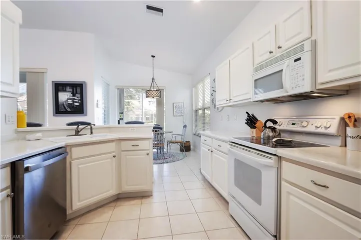 Kitchen featuring white appliances, lofted ceiling, light tile patterned floors, light countertops, and white cabinetry