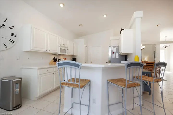 Kitchen with white microwave, a kitchen bar, light tile patterned floors, freestanding refrigerator, and recessed lighting
