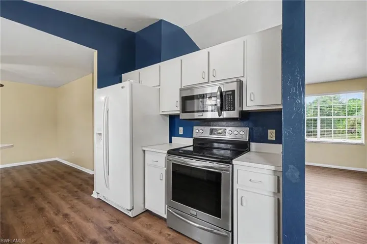 Kitchen featuring white cabinetry, stainless steel microwave, stainless steel electric range, white countertops, and wood-finish flooring