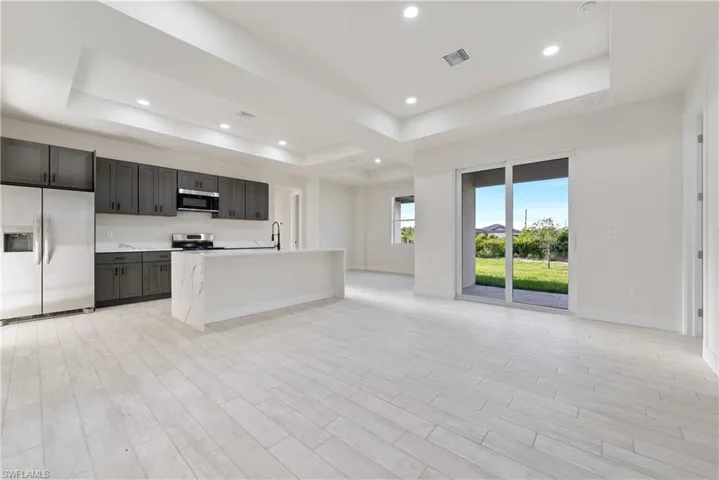 Kitchen featuring a raised ceiling, stainless steel appliances, wood finish floors, a kitchen island with sink, and open floor plan