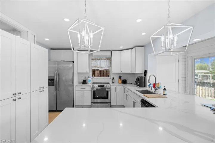 Kitchen featuring pendant lighting, light stone counters, stainless steel appliances, and white cabinets