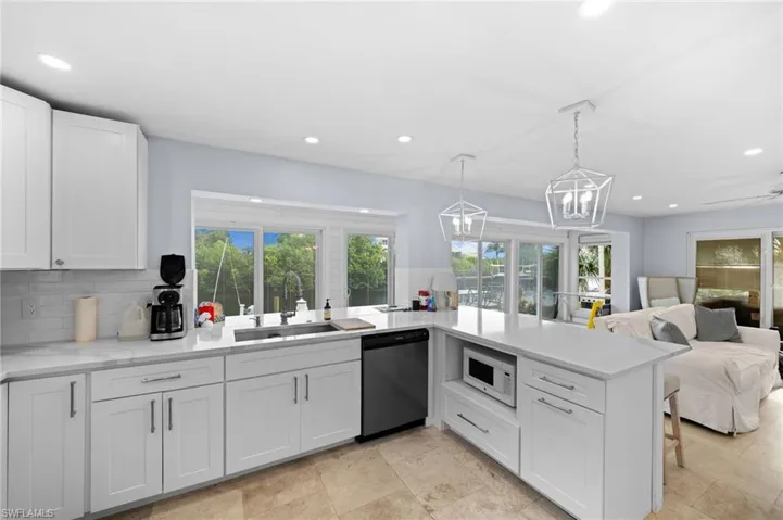 Kitchen with hanging light fixtures, sink, backsplash, white cabinetry, and dishwasher