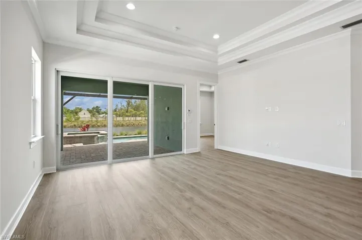 Empty room with a tray ceiling, crown molding, and wood-type flooring
