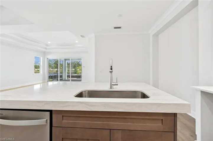 Kitchen featuring light stone countertops, sink, dishwasher, and crown molding