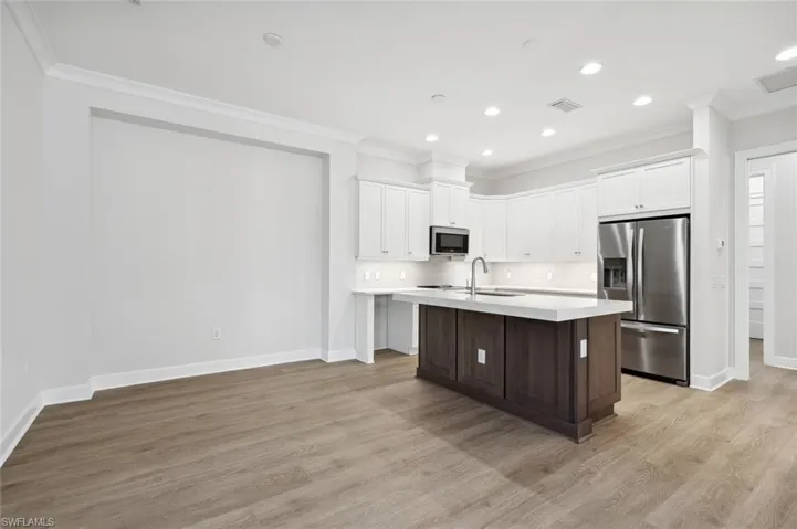 Kitchen featuring appliances with stainless steel finishes, tasteful backsplash, light wood-type flooring, and an island with sink