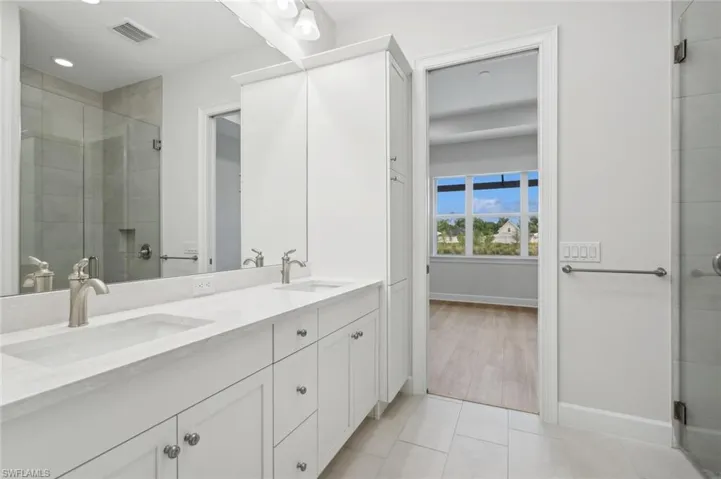 Bathroom with an enclosed shower, tile flooring, and dual bowl vanity