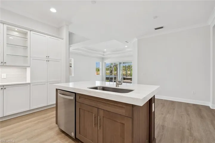 Kitchen with white cabinets, light hardwood / wood-style floors, dishwasher, a center island with sink, and sink