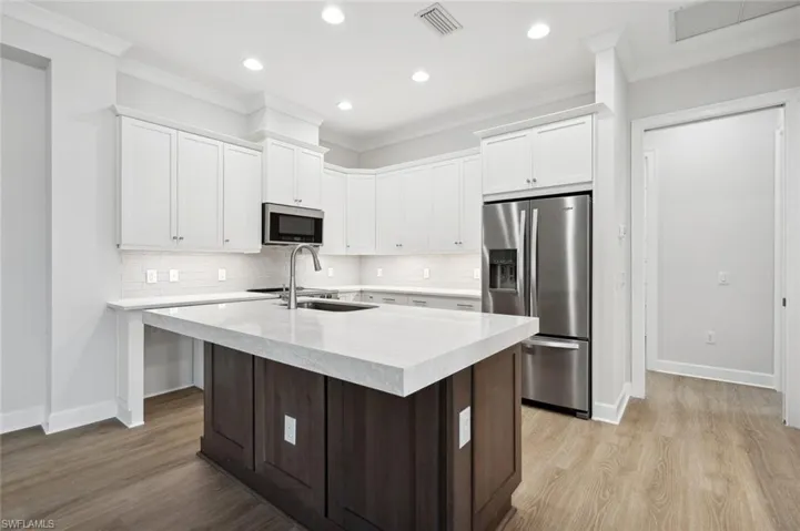Kitchen featuring crown molding, tasteful backsplash, an island with sink, light wood-type flooring, and appliances with stainless steel finishes