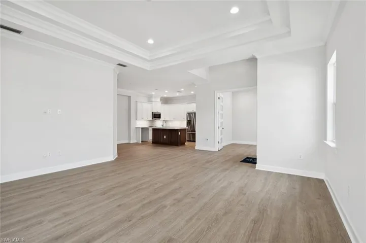 Unfurnished living room with a tray ceiling, sink, ornamental molding, and light hardwood / wood-style floors