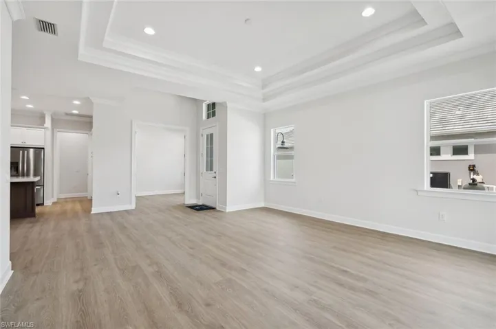 Unfurnished living room with a raised ceiling, light hardwood / wood-style floors, and ornamental molding