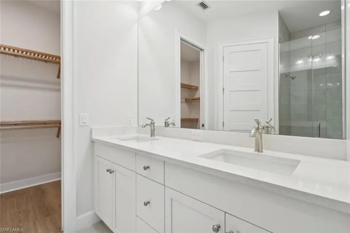 Bathroom featuring a shower with shower door, dual vanity, and hardwood / wood-style flooring