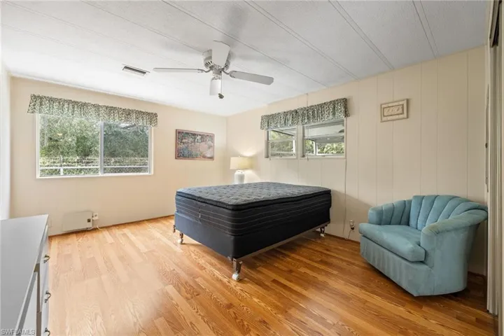 Bedroom with light wood-type flooring, ceiling fan, and wooden walls