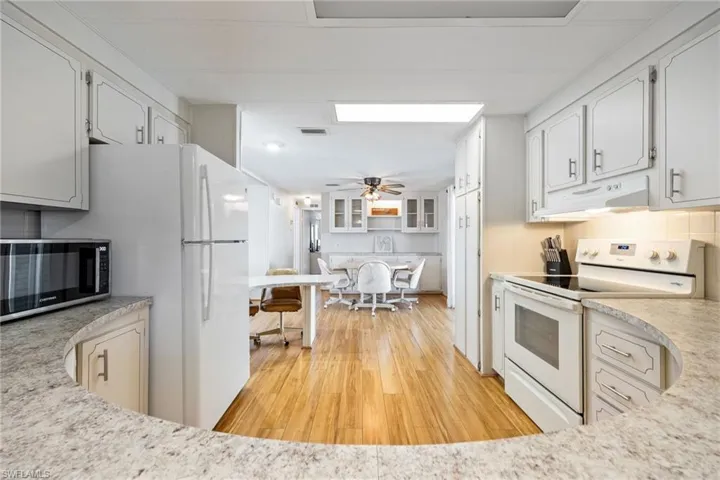 Kitchen with white appliances, light wood finished floors, ceiling fan, under cabinet range hood, and white cabinets
