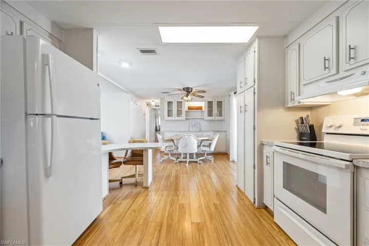 Kitchen featuring white appliances, under cabinet range hood, light wood-style floors, light countertops, and white cabinets
