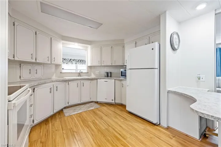 Kitchen featuring white appliances, light countertops, light wood-style floors, and white cabinets