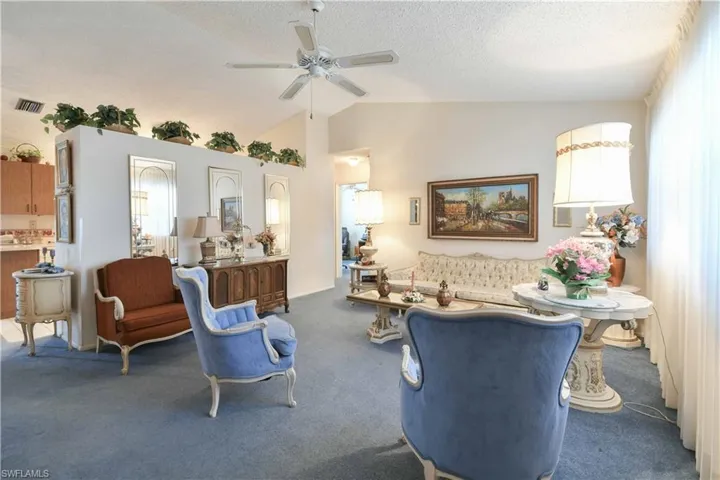 Living room featuring carpet, ceiling fan, vaulted ceiling, and a textured ceiling
