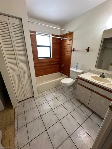 Full bathroom with shower / bathtub combination, toilet, tile patterned floors, vanity, and wood walls