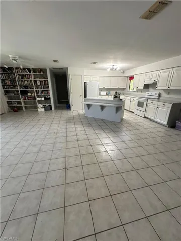 Kitchen featuring light tile patterned flooring, a breakfast bar area, white cabinets, and white appliances