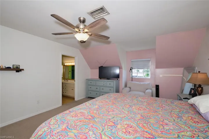 Bedroom featuring light carpet, connected bathroom, vaulted ceiling, and ceiling fan
