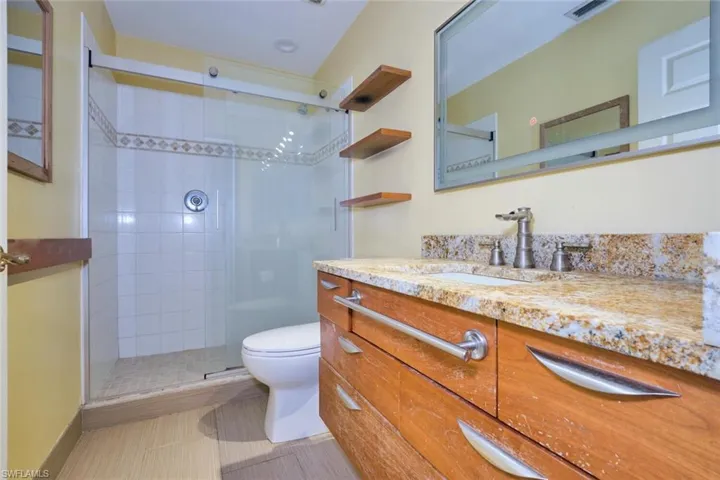 Bathroom featuring vanity, a shower with shower door, toilet, and tile patterned flooring