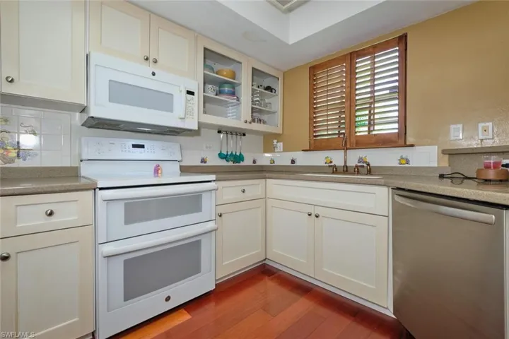 Another view of the kitchen featuring decorative backsplash, white cabinetry, wood-style flooring, and sunken sink.