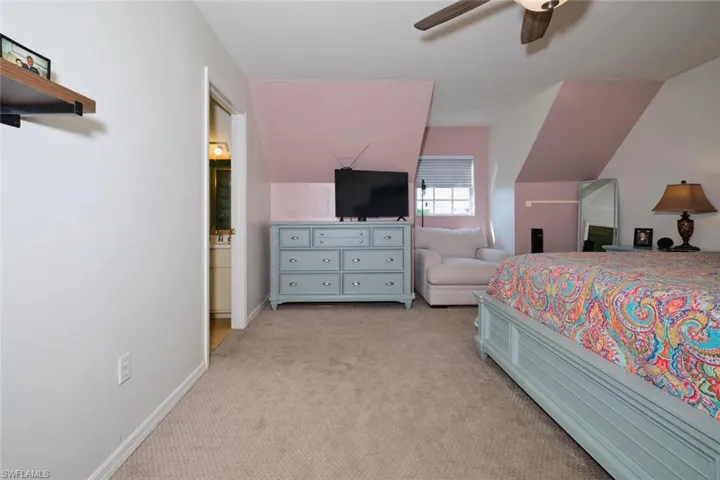 Bedroom with light carpet, vaulted ceiling, ensuite bath, and ceiling fan