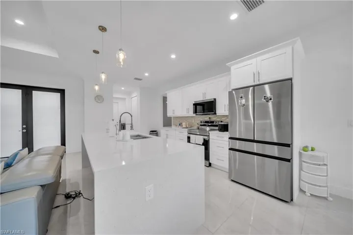 Kitchen featuring stainless steel appliances, decorative light fixtures, white cabinetry, light stone counters, and decorative backsplash