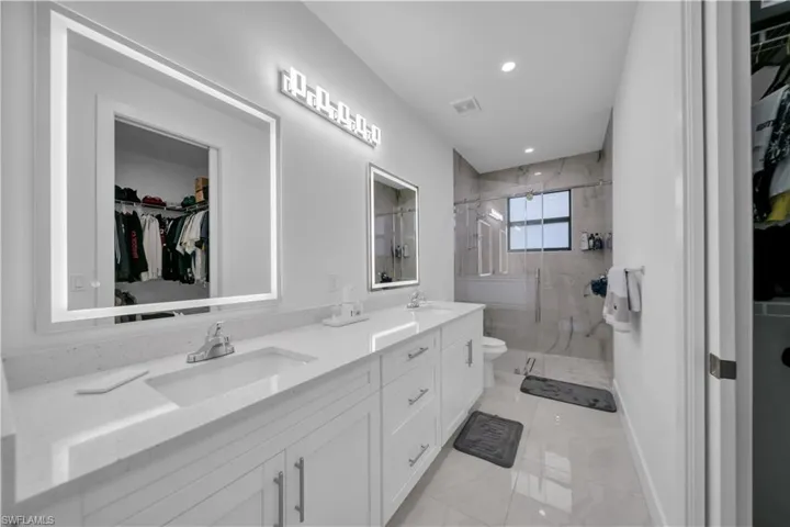 Bathroom with a walk in closet, a marble finish shower, double vanity, and recessed lighting