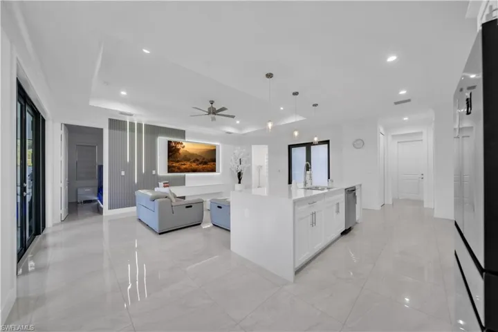 Kitchen featuring open floor plan, white cabinets, light stone countertops, an island with sink, and fridge
