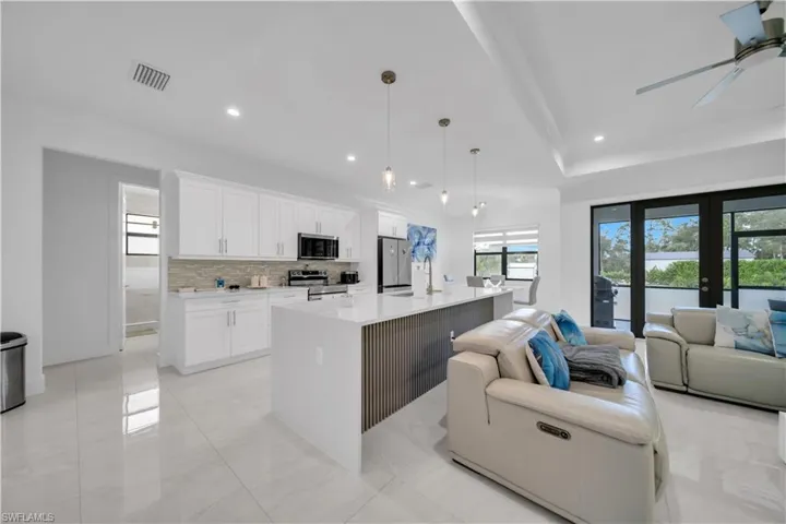 Kitchen featuring open floor plan, decorative light fixtures, white cabinets, a kitchen island with sink, and plenty of natural light