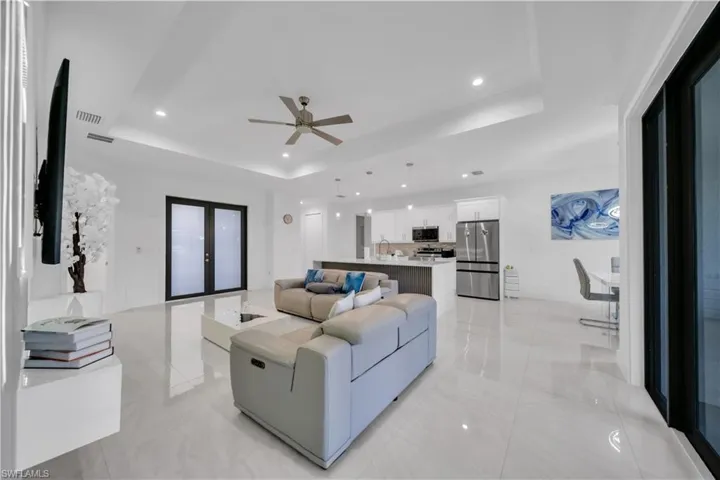 Living area featuring french doors, a tray ceiling, ceiling fan, and recessed lighting