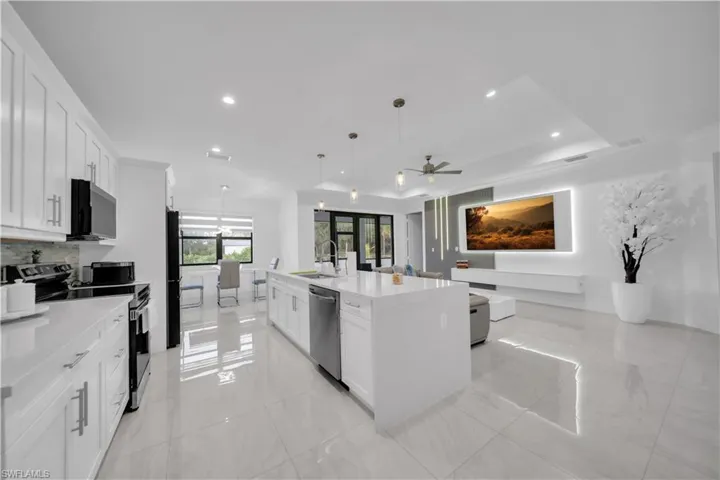 Kitchen featuring appliances with stainless steel finishes, white cabinetry, a kitchen island with sink, hanging light fixtures, and light stone counters