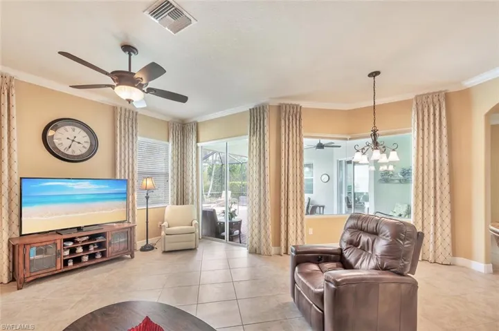 Living area featuring ornamental molding, plenty of natural light, light tile patterned flooring, a ceiling fan, and a chandelier