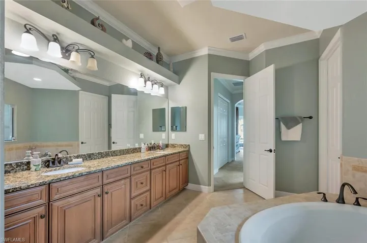 Bathroom with double vanity, a bath, crown molding, and light tile patterned floors