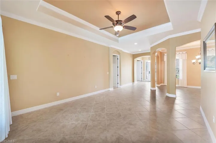Unfurnished room with a raised ceiling, light tile patterned floors, crown molding, ceiling fan, and arched walkways
