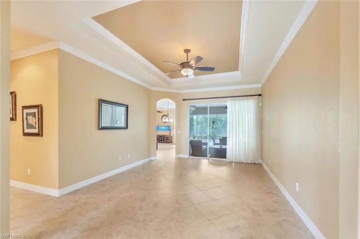 Empty room featuring a raised ceiling, arched walkways, crown molding, light tile patterned floors, and a ceiling fan