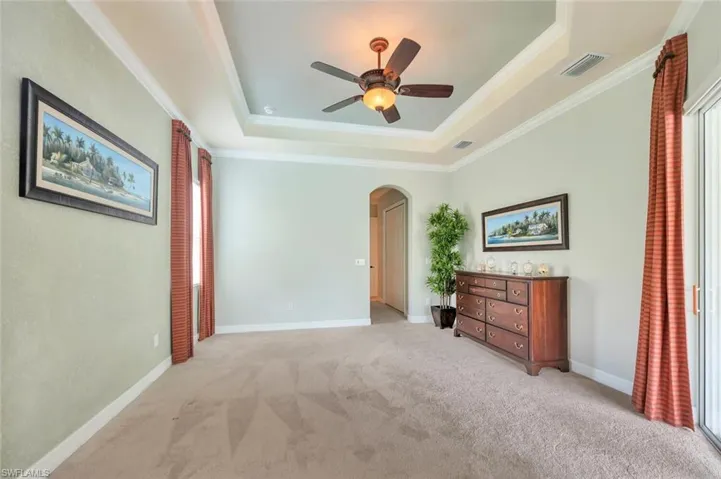 Carpeted spare room featuring arched walkways, a raised ceiling, crown molding, and a ceiling fan