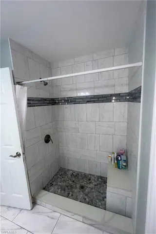 Walk-in shower featuring light-toned rectangular wall tiles, a decorative glass tile accent band, a pebble-stone shower floor, a built-in shower bench, and a bronze-finish shower fixture