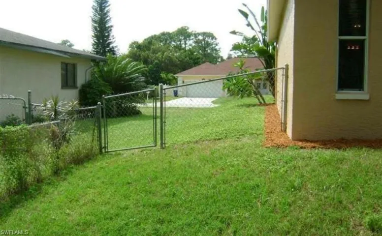 Grassy yard space featuring a chain-link fence with gate and mature landscaping