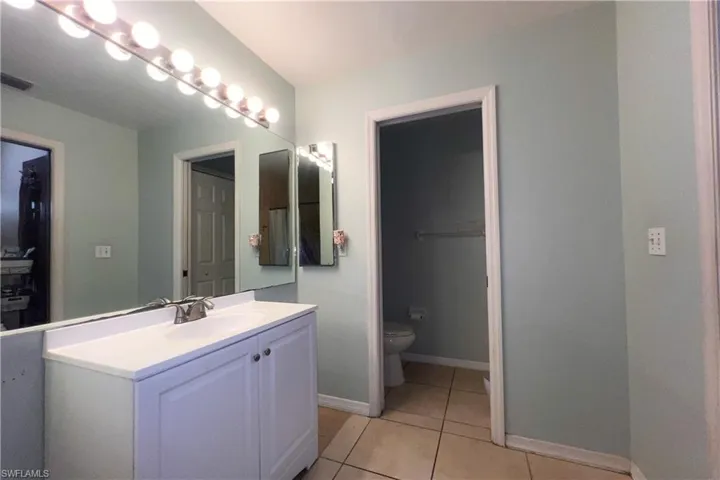 Bathroom featuring a vanity with a white countertop and base cabinetry, a large wall-mounted mirror, and tile flooring
