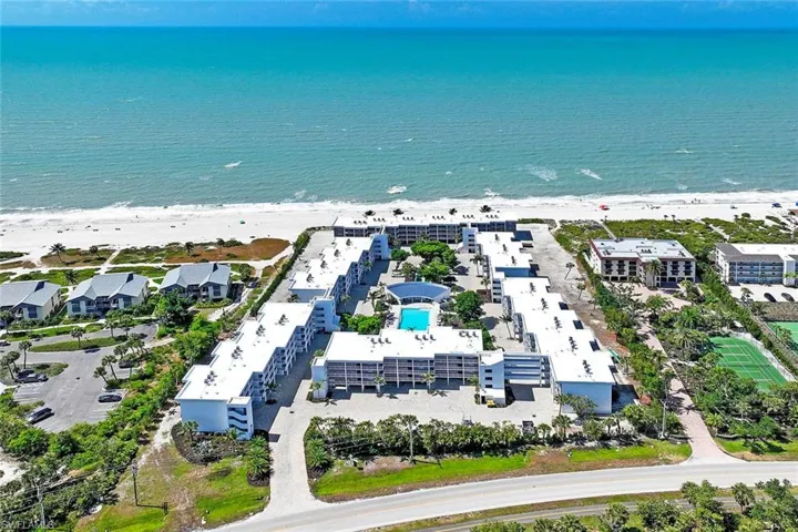 Beachfront resort-style community featuring multiple residential buildings with contemporary architecture, a central courtyard with resort-style pool and spa, manicured landscaping with mature trees, and direct beach access overlooking the Atlantic Ocean
