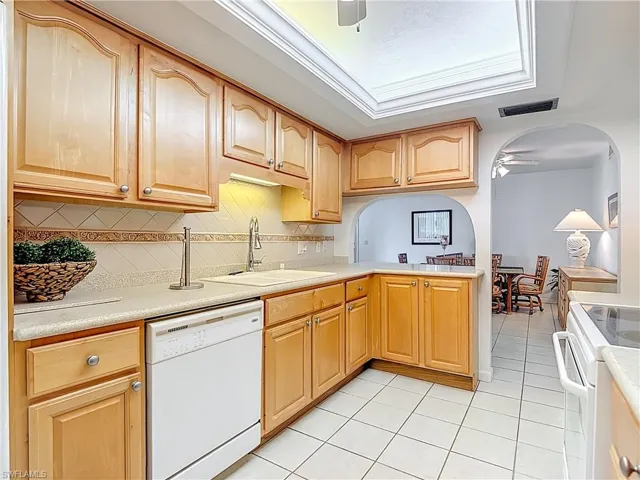 Kitchen with ceiling fan, white appliances, light tile patterned floors, light countertops, and arched walkways