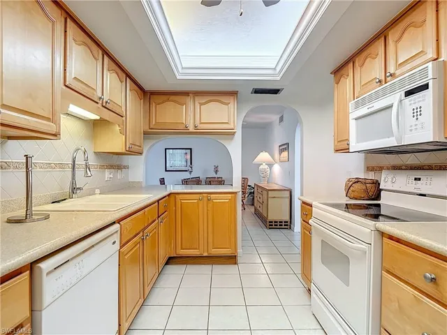 Kitchen featuring decorative backsplash, white appliances, arched walkways, and light tile patterned floors