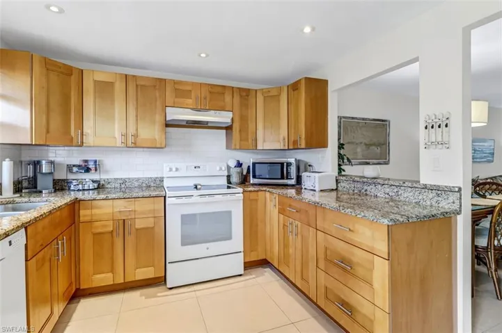 Kitchen featuring white appliances, under cabinet range hood, decorative backsplash, light stone countertops, and recessed lighting