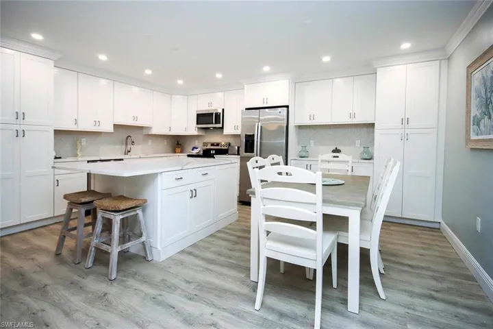 Kitchen featuring light wood-LVP flooring, stainless steel appliances, white cabinetry, and a kitchen island