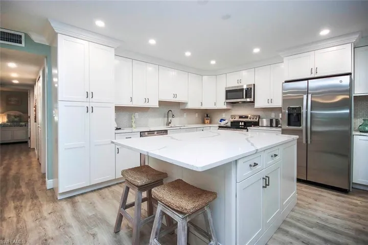 Kitchen appliances with stainless steel finishes, a center island, and white cabinetry