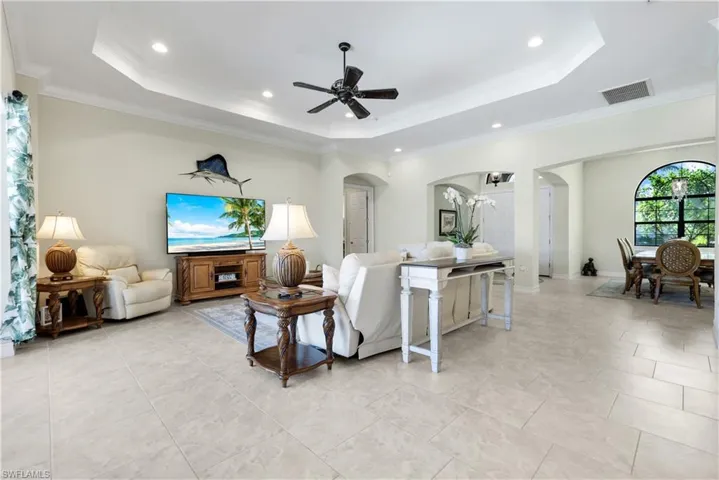 Living area featuring a raised ceiling, arched walkways, crown molding, light tile patterned flooring, and a ceiling fan