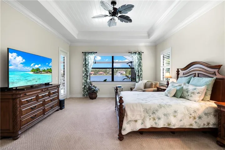Bedroom featuring light colored carpet, multiple windows, ornamental molding, a raised ceiling, and a ceiling fan