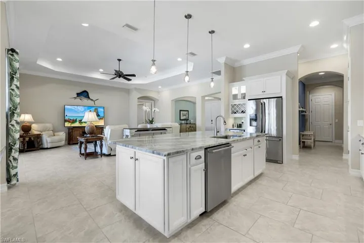 Kitchen featuring arched walkways, white cabinetry, appliances with stainless steel finishes, open floor plan, and hanging light fixtures